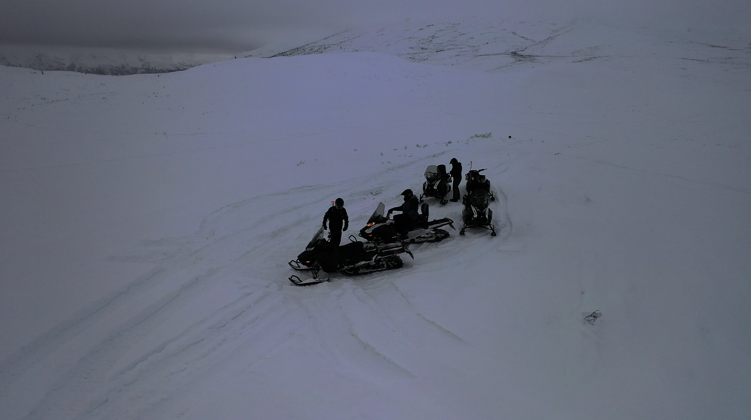 a group of snowmobilers gather in a snowfield in Alaska